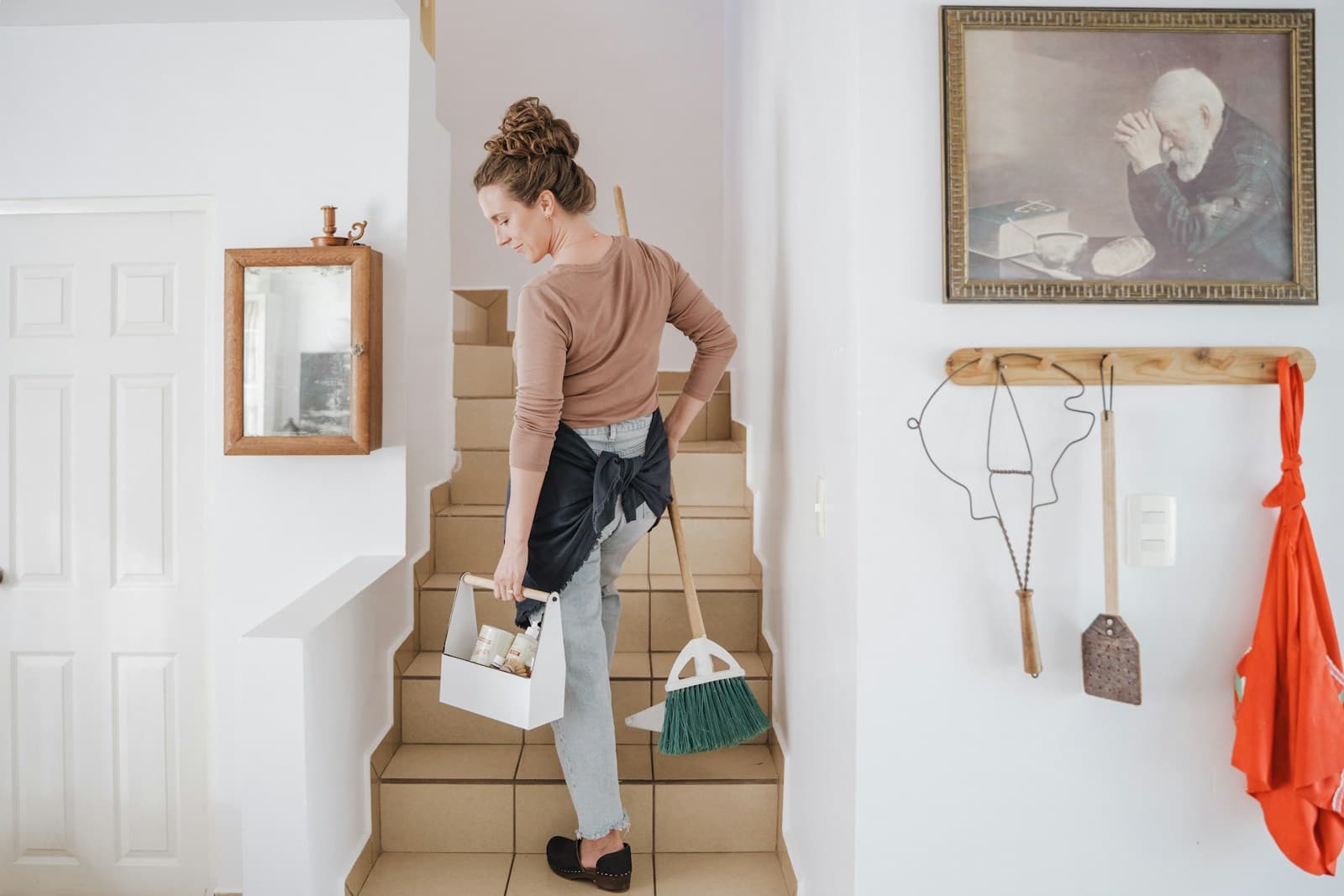 A cleaner carrying her caddy and broom up the stairs of a home